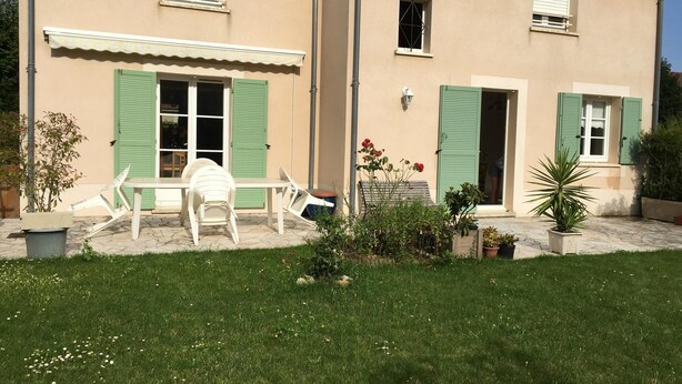 A two-story house with a patio area featuring a table and chairs, a small garden with potted plants, and a well-maintained lawn. - Beautiful house with large garden near Disneyland (Bussy-Saint-Georges)