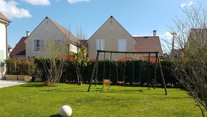 A grassy backyard with a swing set, a white ball, and a house with a brown roof. - Beautiful house with large garden near Disneyland (Bussy-Saint-Georges)