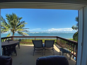 Uma varanda com vista para o oceano, duas cadeiras, uma mesa e um pequeno banco.