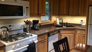 Una cocina con gabinetes de madera, estufa, microondas, cafetera y lavaplatos.