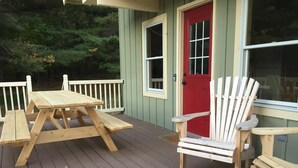 Una terraza de madera con una mesa de picnic y dos sillas Adirondack.