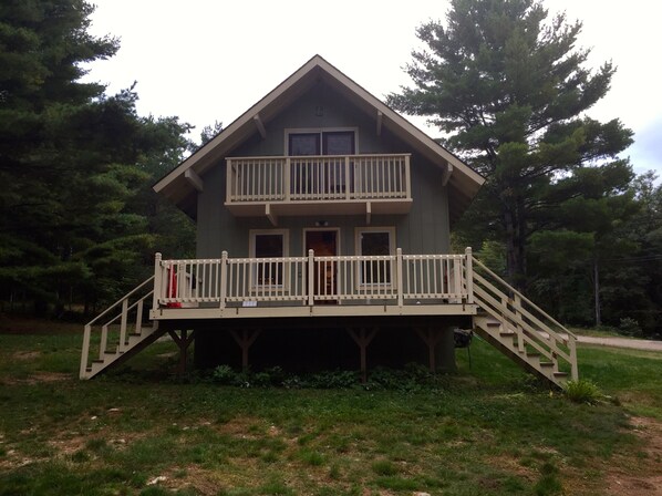 A two-story cabin with a balcony, surrounded by trees.
