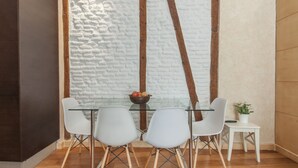 A modern dining area with a glass table and white chairs, a white brick wall, and a wooden beam structure. - Luxury Apart. Centro, Barrio Letras, Walk to Museums, Plazas and GranVia.  . (Madrid)