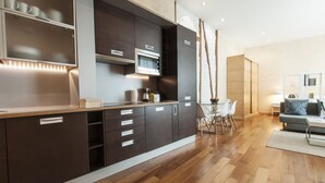 A modern kitchen with dark cabinetry, a built-in oven, and a dining area with a white table and chairs. - Luxury Apart. Centro, Barrio Letras, Walk to Museums, Plazas and GranVia.  . (Madrid)