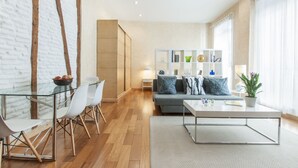 A modern living room with a glass dining table, white chairs, a grey sofa, and a bookshelf. - Luxury Apart. Centro, Barrio Letras, Walk to Museums, Plazas and GranVia.  . (Madrid)