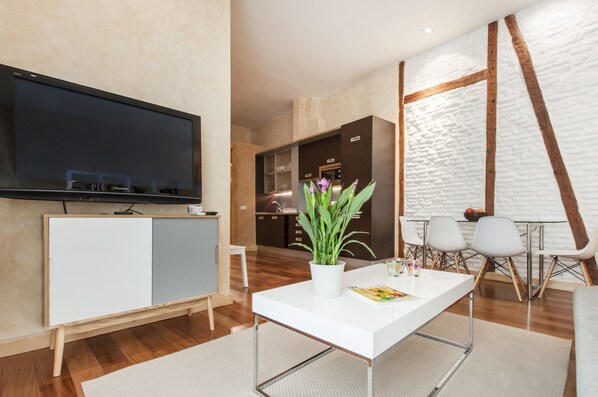 Uma sala de estar moderna com uma televisão de tela plana, uma mesa de jantar branca e um vaso com planta.