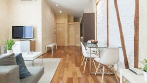 A modern living room with a flat-screen TV, a sofa, a dining table with chairs, and a kitchen area with a stove and cabinets. - Luxury Apart. Centro, Barrio Letras, Walk to Museums, Plazas and GranVia.  . (Madrid)