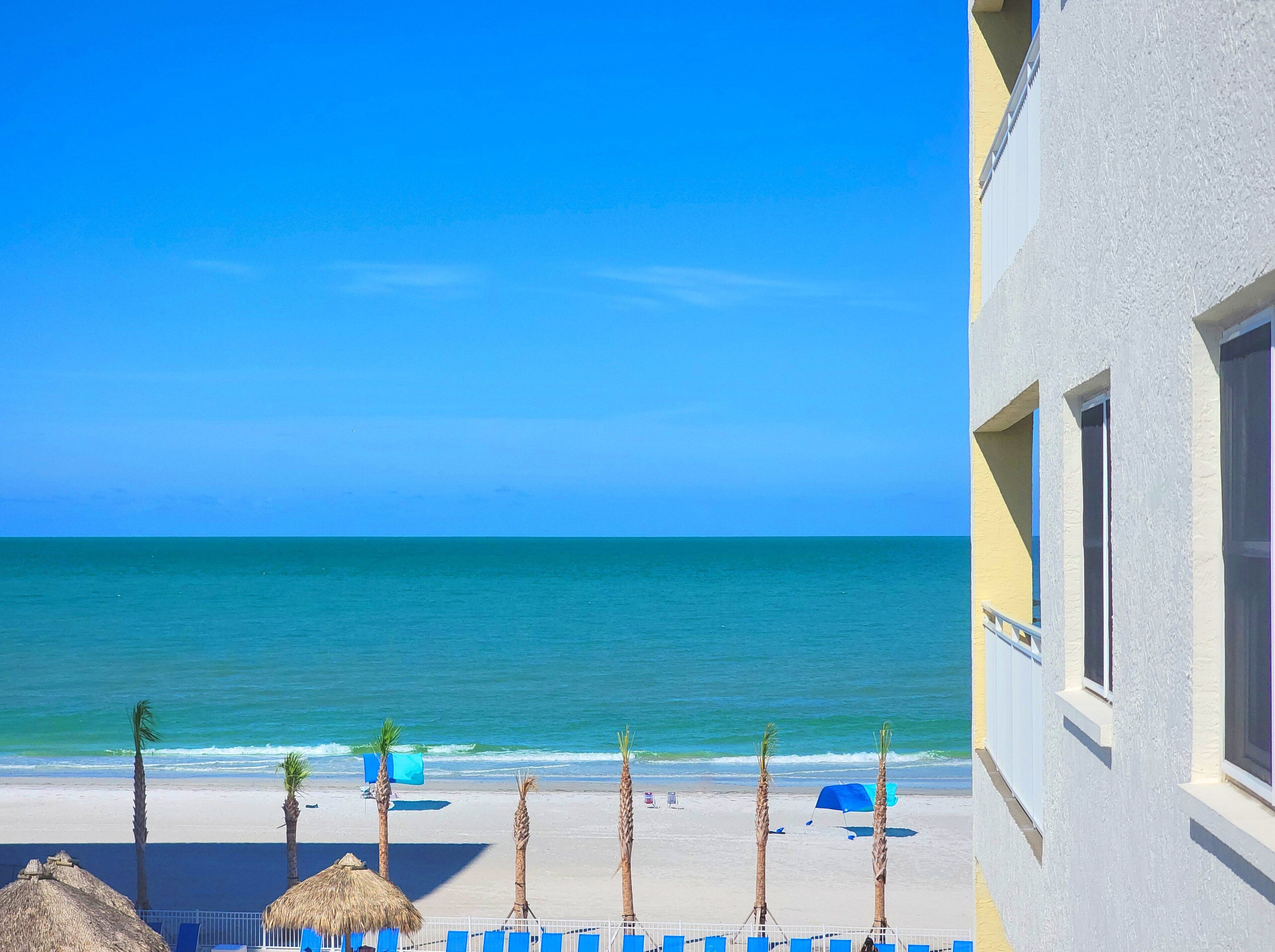 A beach view with a clear sky, a sandy beach, and a building with a white facade.