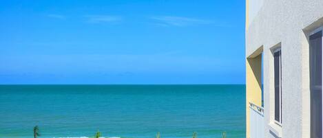 Vista de la playa con cielo despejado, arena dorada y un edificio de fachada blanca.