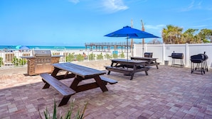 An outdoor patio with picnic tables, a grill, and a view of the ocean.