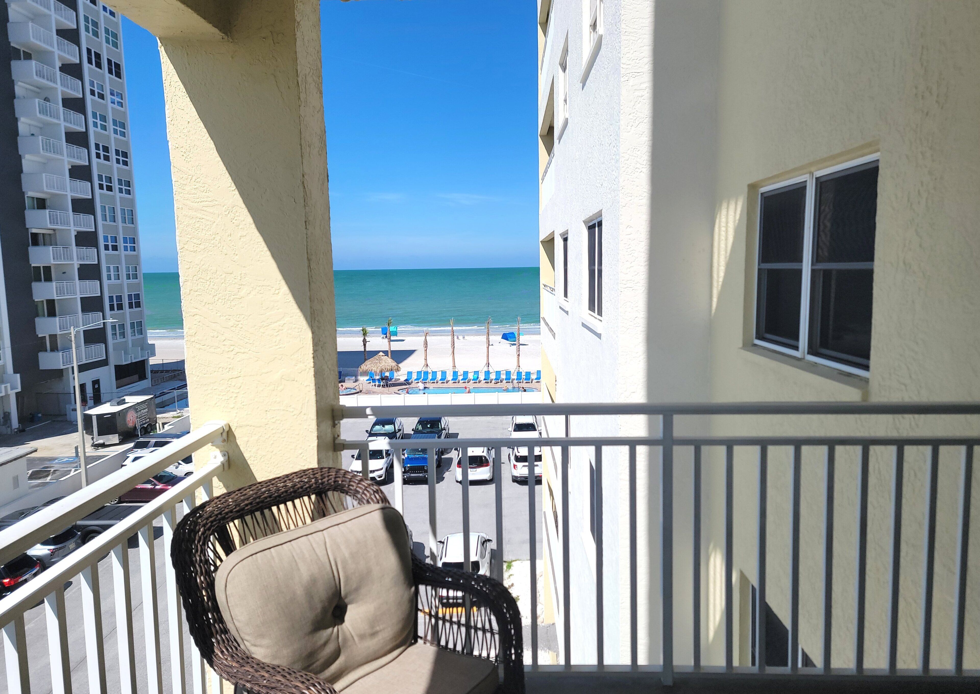 Un balcon avec vue sur l’océan, une chaise et un bâtiment doté d’une piscine et de chaises longues.