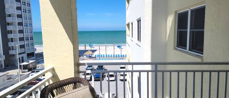 Ein Balkon mit Meerblick, ein Stuhl und ein Gebäude mit Pool und Liegestühlen.