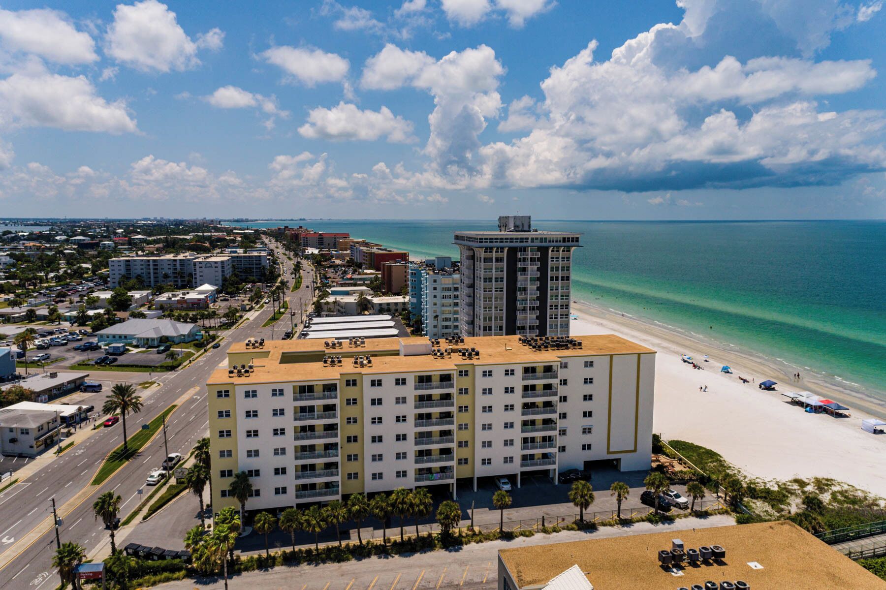 A multi-story hotel with a beach view, located near a coastal road with palm trees and a parking lot.