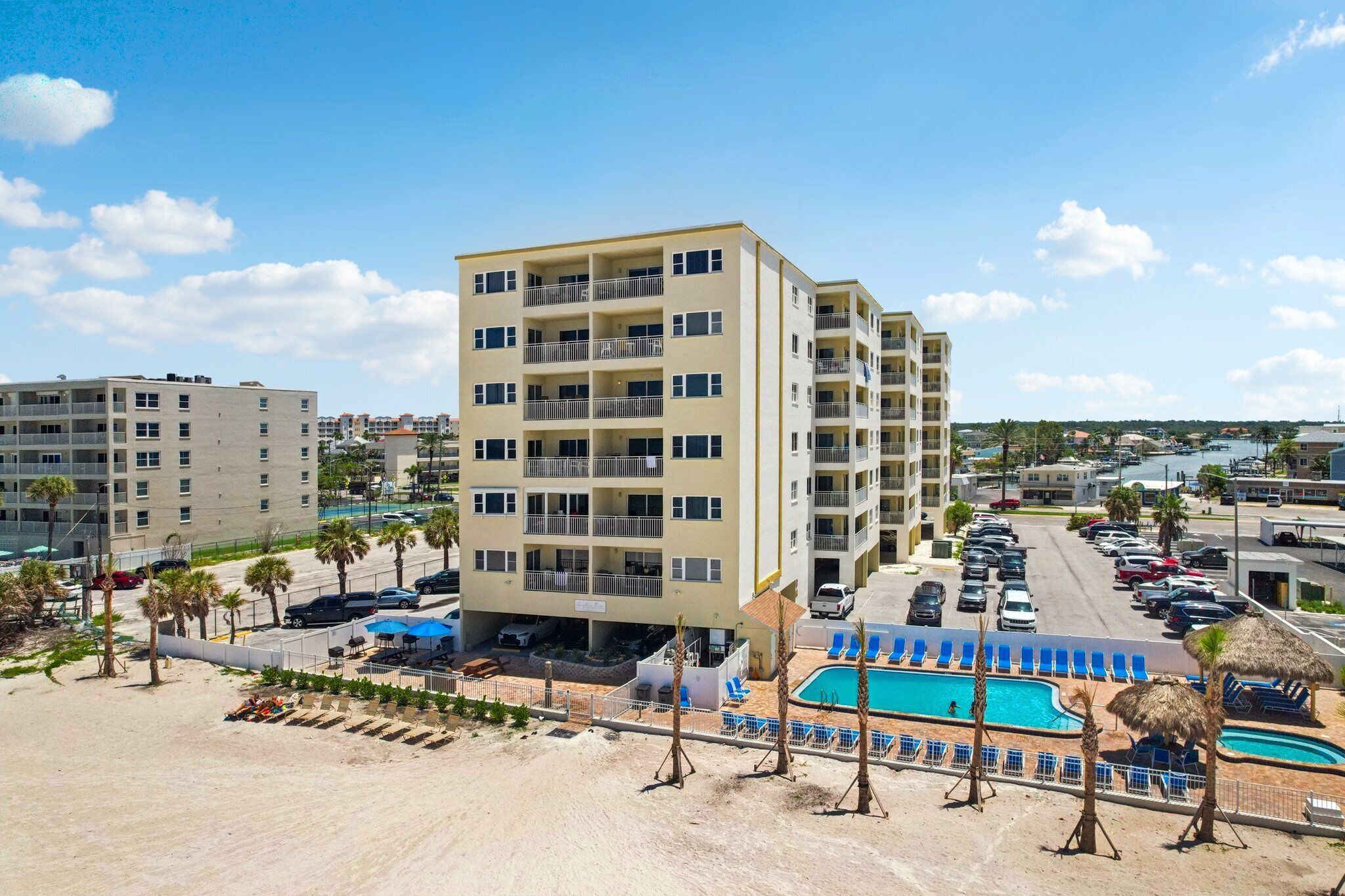 Ein mehrstöckiges Hotel mit Poolbereich, Liegestühlen, Sonnenschirmen und einem Strand im Vordergrund.