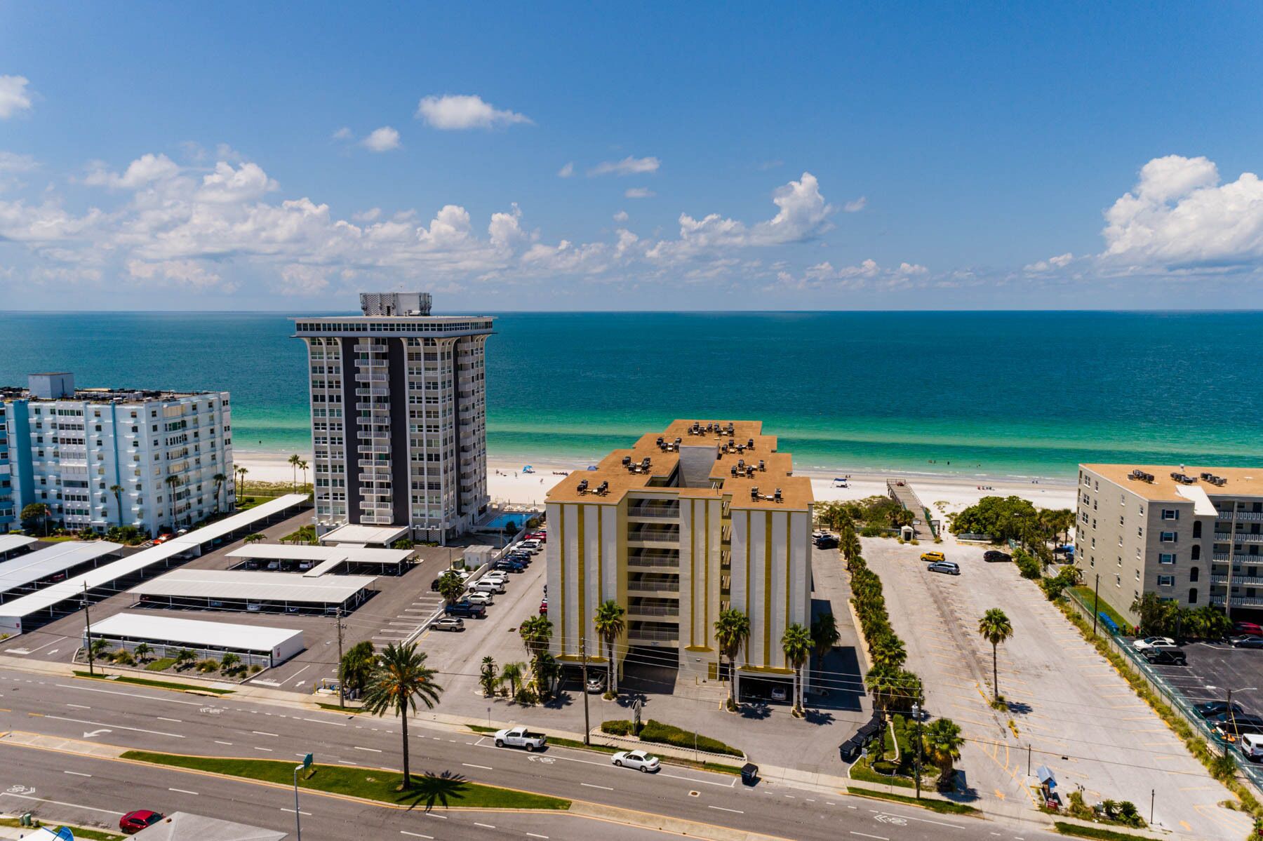 Un hôtel de grande hauteur doté d’une piscine sur le toit et offrant une vue sur la plage, situé à côté d’un parking et d’une route.