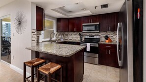 A modern kitchen with dark wood cabinets, stainless steel appliances, a granite countertop, and a large island with bar stools.