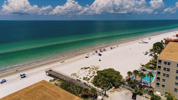 A beach with a clear view of the ocean, a sandy shore, and a building with a pool.