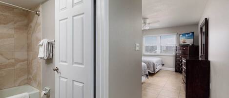 A bathroom with a bathtub and a shower, a bedroom with a bed and a dresser, and a living area with a television.