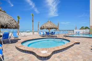 Et poolområde med liggestole, et spabad og en stråtækt parasol.