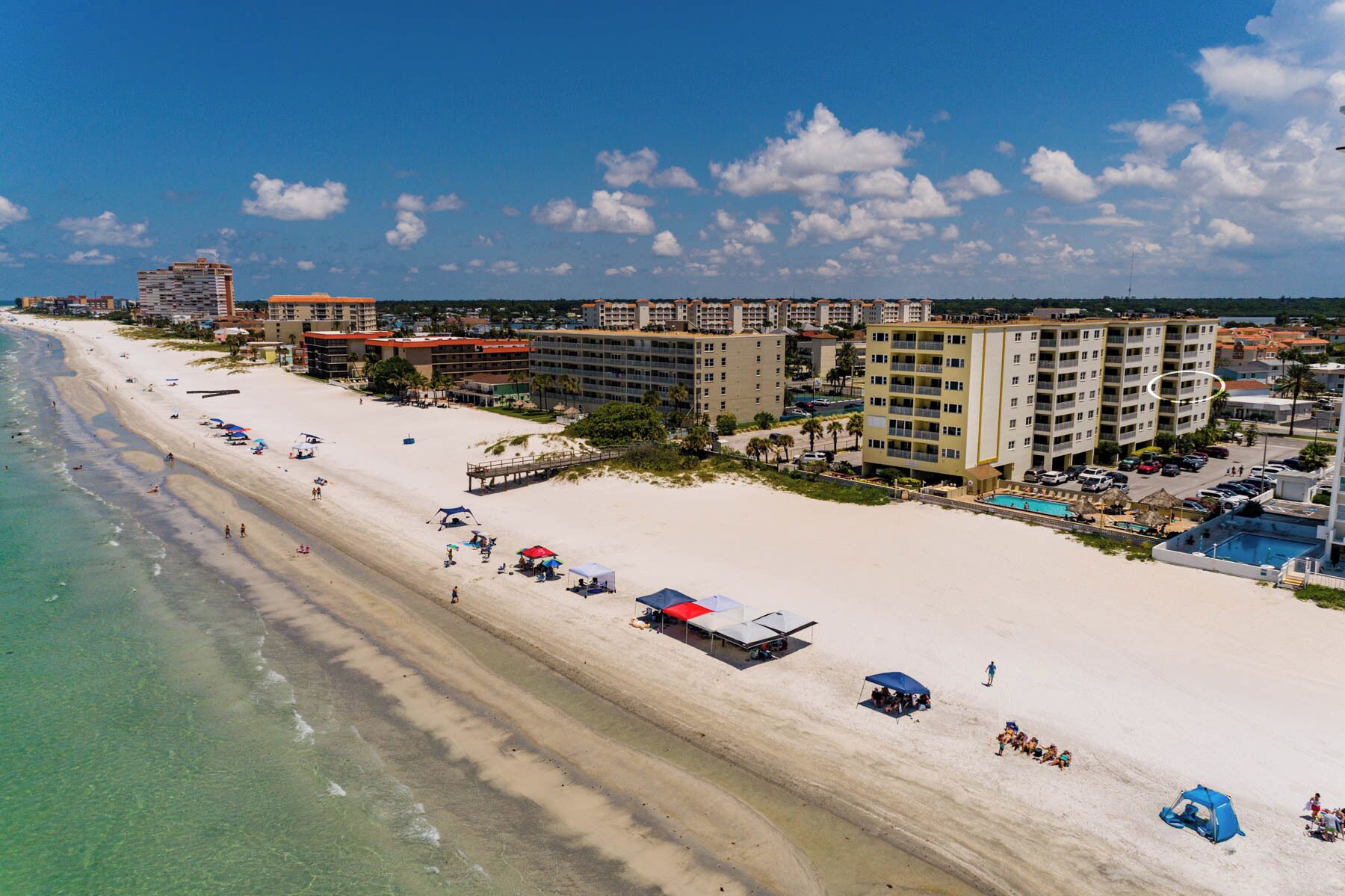 Un hotel frente a la playa con varias construcciones, una playa de arena y un cielo azul despejado.
