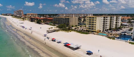 Un hotel frente a la playa con varias construcciones, una playa de arena y un cielo azul despejado.