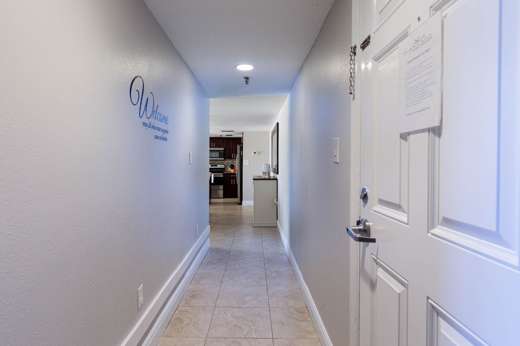 Un pasillo con un cartel de 'Welcome', una zona de cocina y una puerta con cerradura.