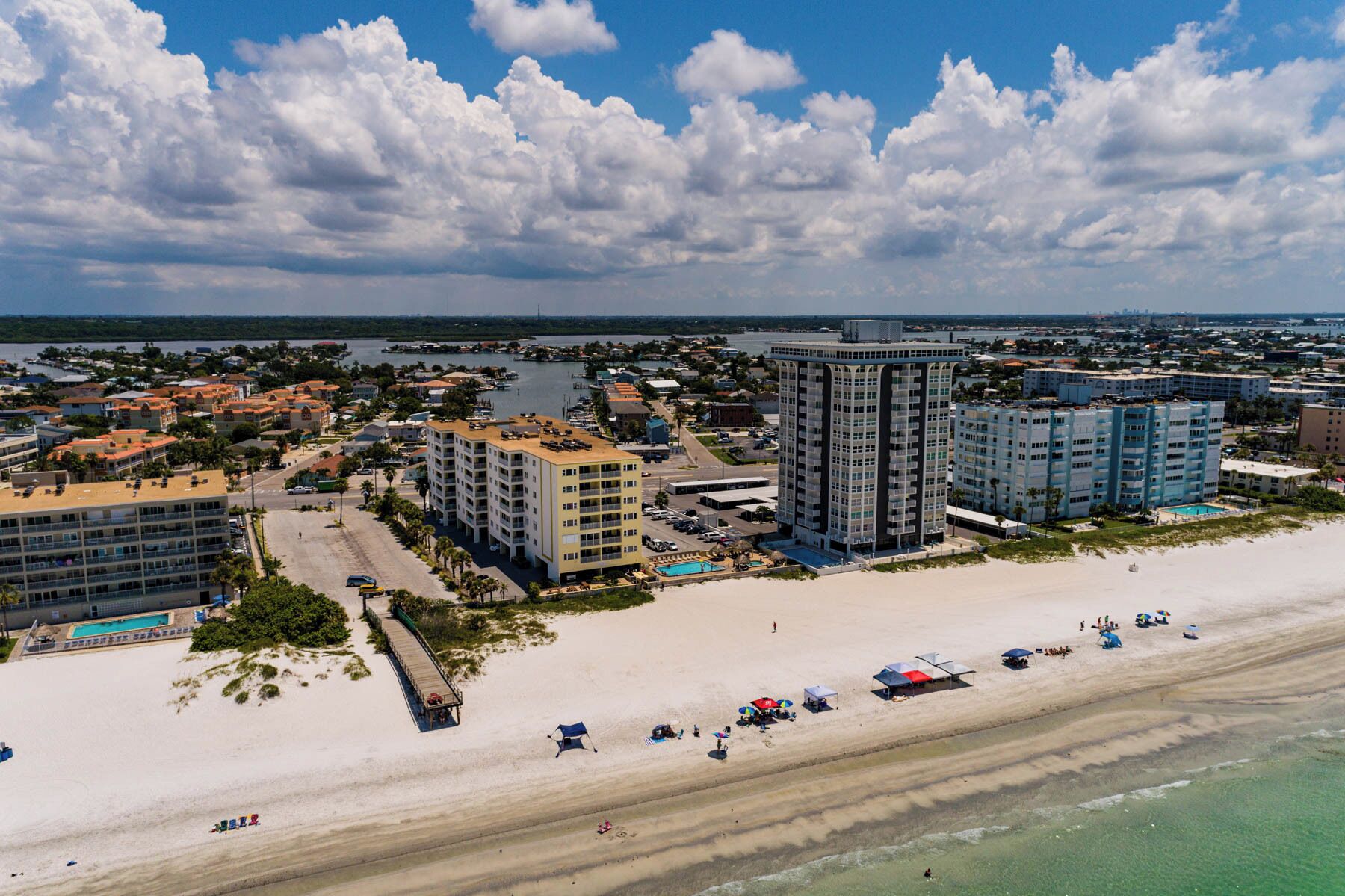 An aerial view of a coastal area with a beach, a marina, and several high-rise buildings.