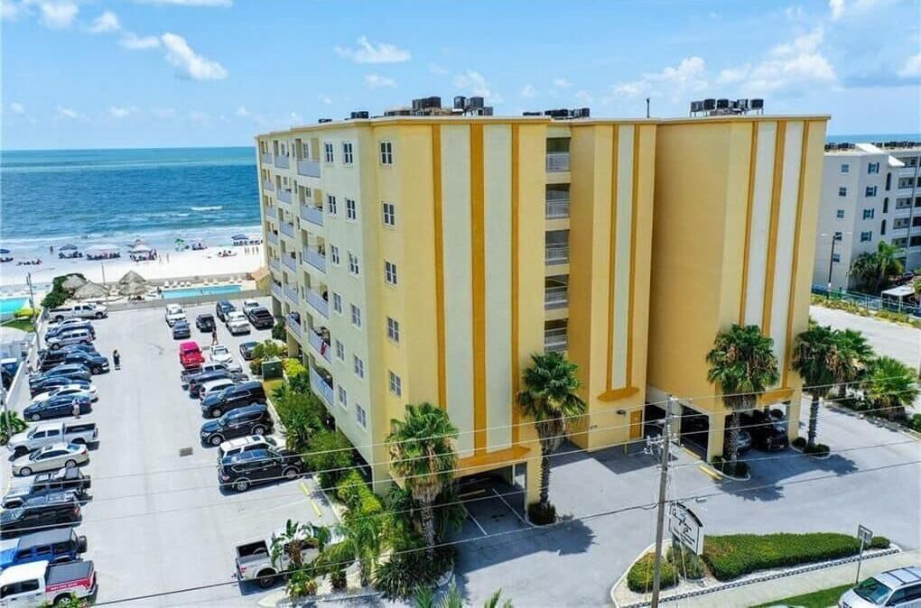 A multi-story hotel with a yellow facade, a parking lot, and a view of the beach.