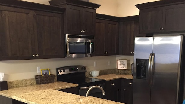 Una cocina con armarios de madera oscura, un refrigerador de acero inoxidable, un microondas y una encimera de granito. Hay dos taburetes color turquesa en la isla.