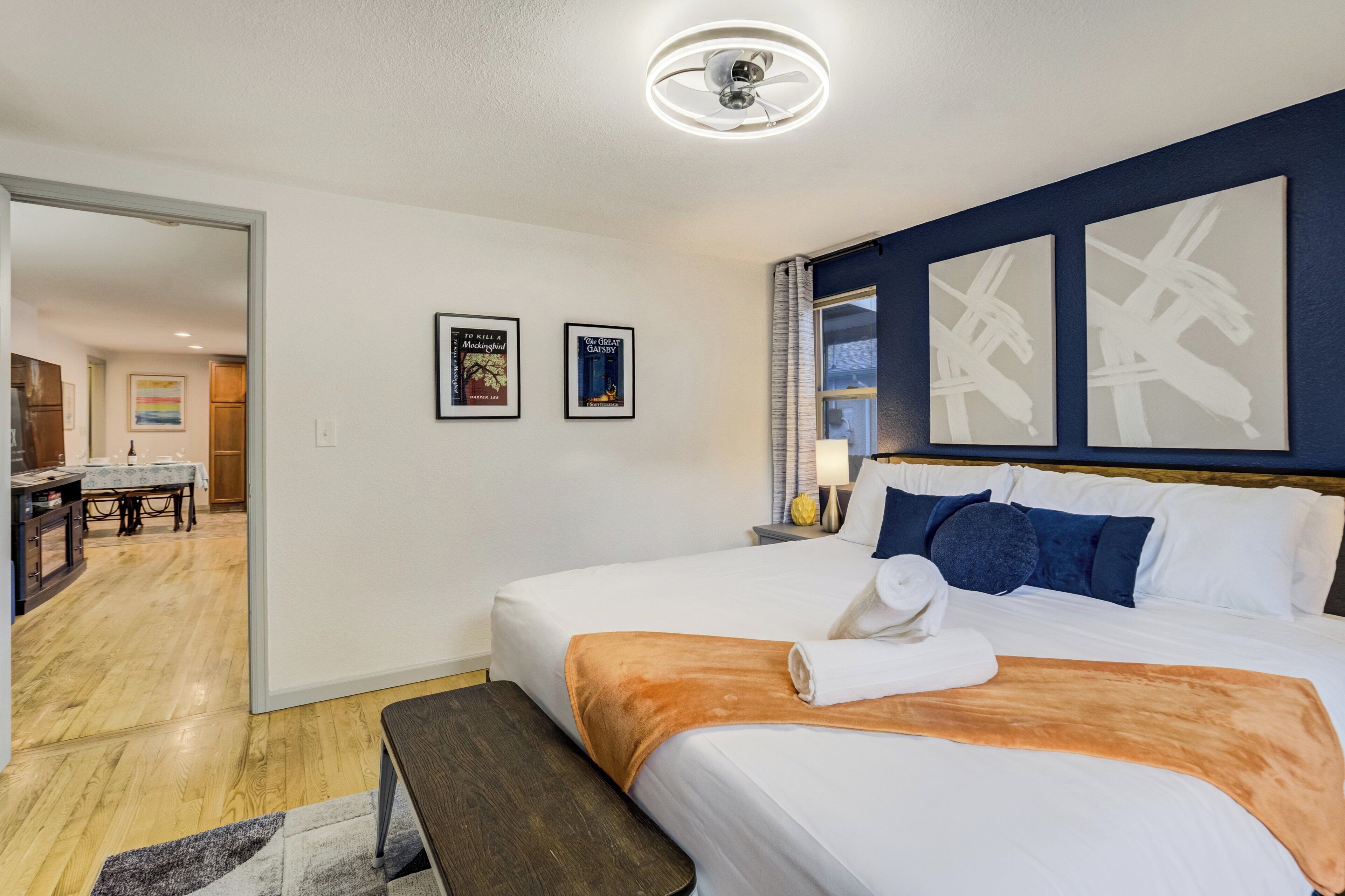 Ett hotellrum med en säng, en bänk, ett skrivbord och en stol. Det finns två inramade tavlor på väggen.