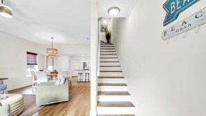 Un interior moderno con una escalera, una zona de comedor y una sala de estar con sofá y reposapiés.