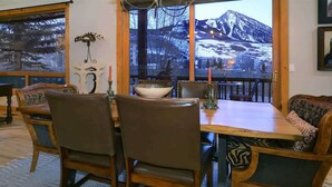 Un coin repas avec une table et des chaises en bois, une grande fenêtre donnant sur les montagnes et un lustre.