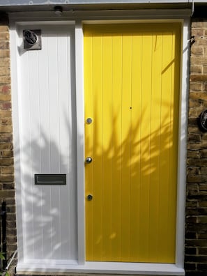 A yellow door with a white door panel, a mailbox, and a small vent on the wall.