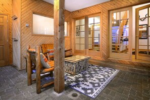 Un intérieur en bois, avec une chaise en bois, une table à plateau en verre et un tapis à motifs.