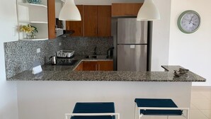 A modern kitchen with granite countertops, stainless steel appliances, wooden cabinets, and two bar stools. - NEW Amazing Ocean View - 301C (boca chica)
