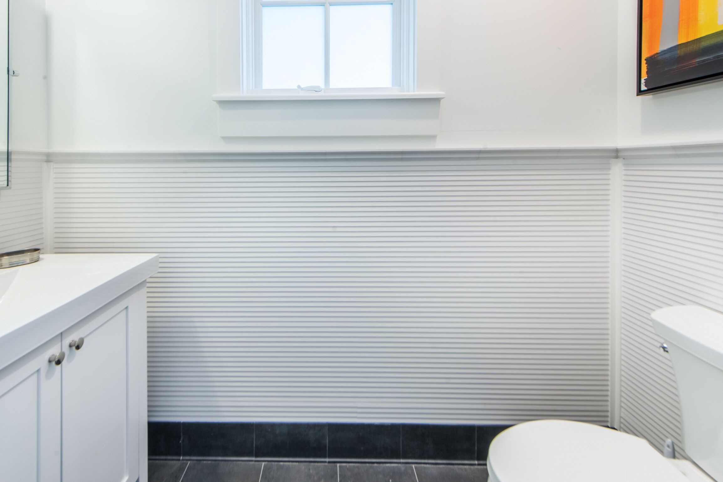 A bathroom with a white vanity, a toilet, and a window above the sink.