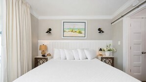 A hotel room with a large bed, two bedside tables with lamps, a framed picture on the wall, and a door to the right. - Great Rates! Two Bedroom ~ Gulf Shores Surf & Racquet (Gulf Shores)