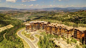 A multi-story hotel with a curved driveway, surrounded by forested hills and mountains.