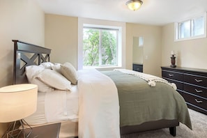 A bedroom with a bed, a nightstand, a lamp, a dresser, and a window with a view of trees.