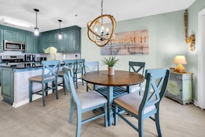 A modern kitchen with teal cabinets, a central island, and a round dining table with chairs.