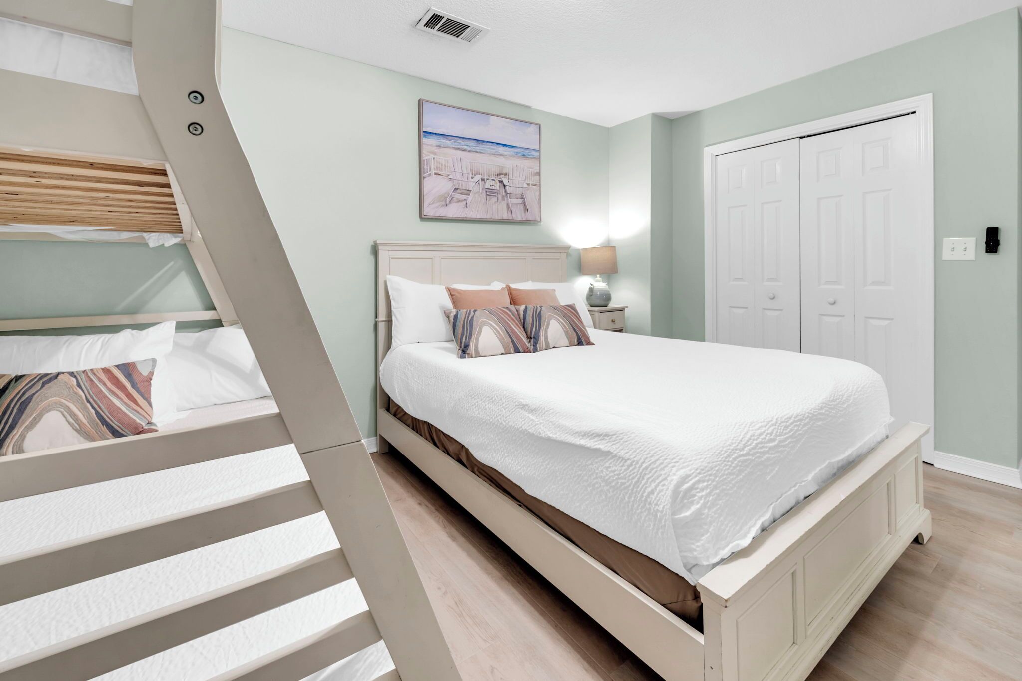 A bedroom with a bed, a nightstand, a lamp, a door, and a painting on the wall.