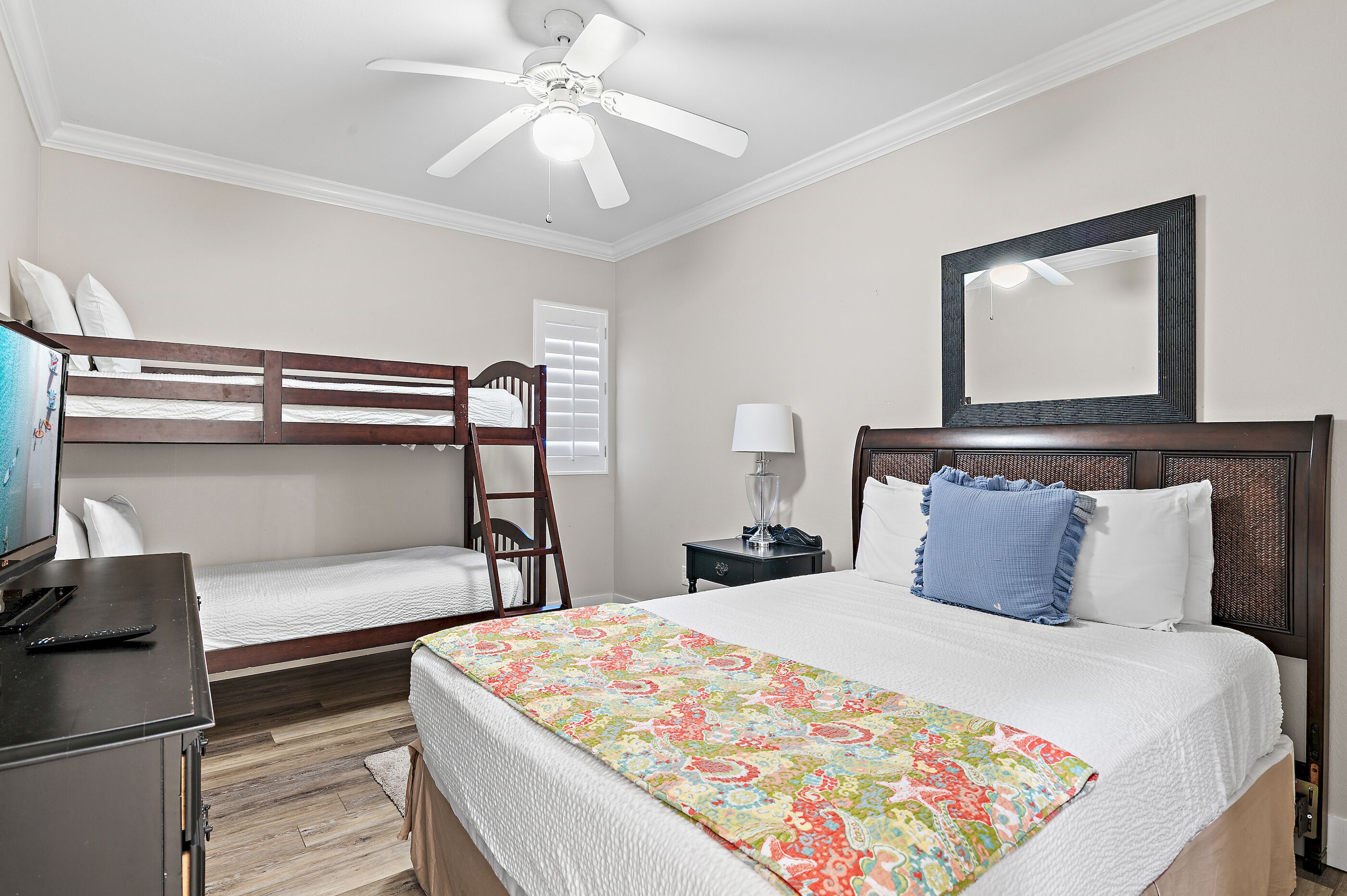 A bedroom with a bunk bed, a single bed, a desk with a computer, a lamp, a ceiling fan, and a mirror.