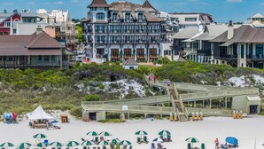 A beachfront hotel with a prominent tower, a wooden boardwalk leading to the beach, and beach umbrellas.