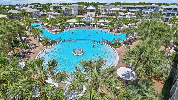 A large outdoor swimming pool surrounded by palm trees and hotel buildings.