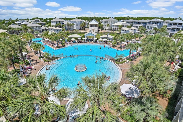 A large outdoor swimming pool surrounded by palm trees and hotel buildings.
