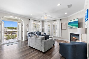A living room with a gray sofa, a blue armchair, a fireplace, and a balcony with white shutters.