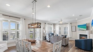 A spacious living area with a wooden dining table, white chairs, a blue sofa, and a fireplace.