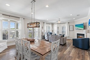 A spacious living area with a wooden dining table, white chairs, a blue sofa, and a fireplace.