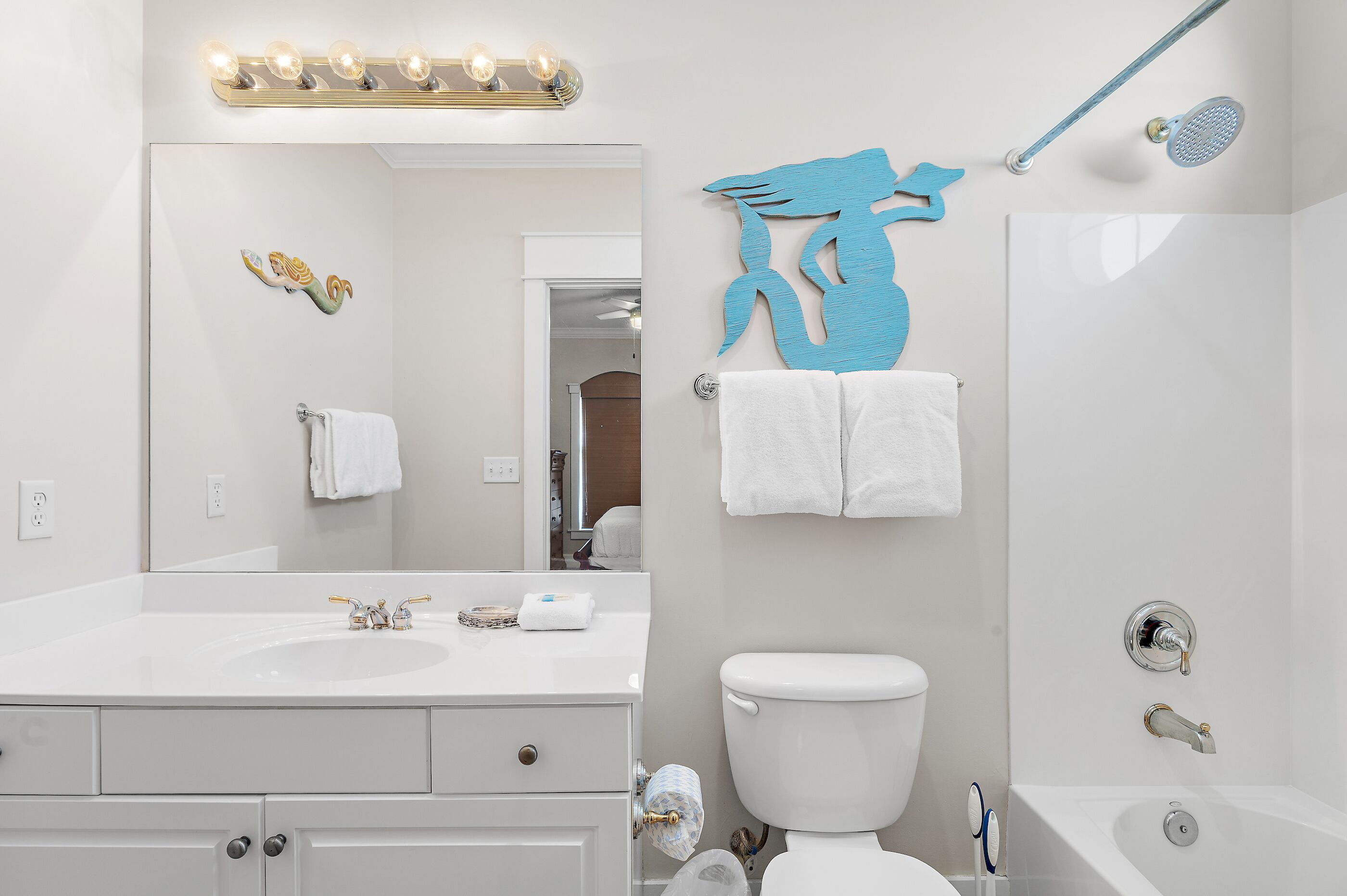 Een badkamer met een wit wastafel, spiegel en toilet, een douchegedeelte, en een handdoekrek met twee handdoeken.