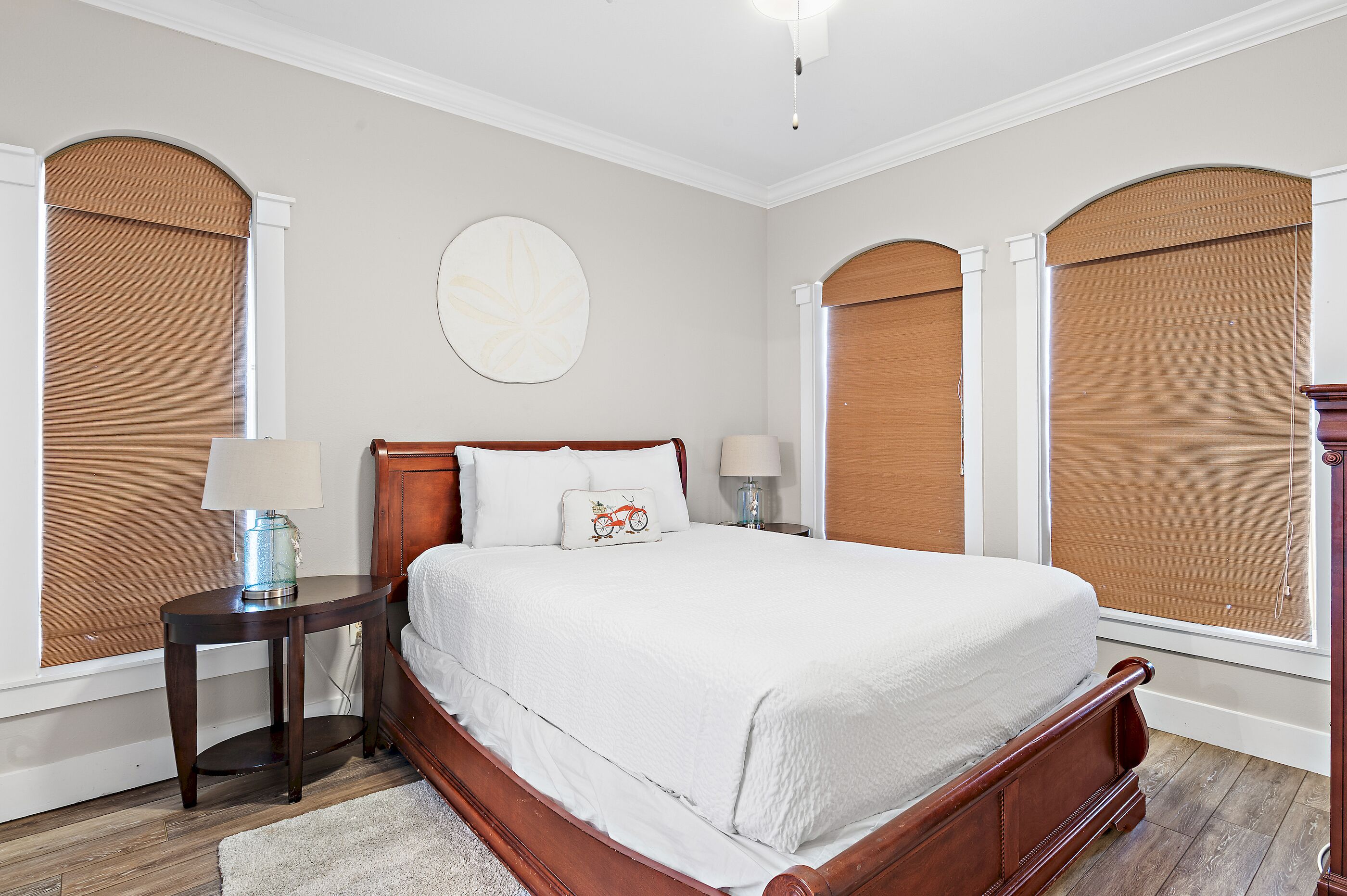 A bedroom with a wooden bed, two bedside tables, a round wall decoration, and a window with a blind.